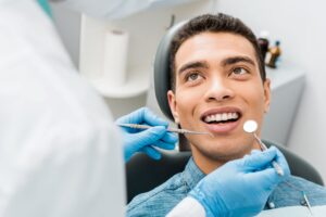 Man with brown eyes in blue shirt looking up at dentist during oral exam