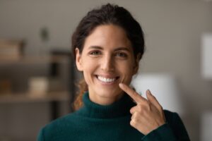 Woman in dark green turtle neck pointing to her smile