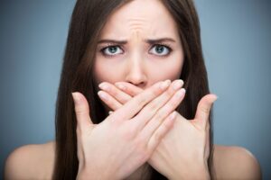 Woman with long brown hair crossing her hands over her mouth with concerned expression